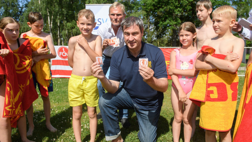Ministerpräsident Dr. Markus Söder, MdL (Mitte), überreicht Kindern das Seepferdchen-Abzeichen im Nürnberger Freibad.