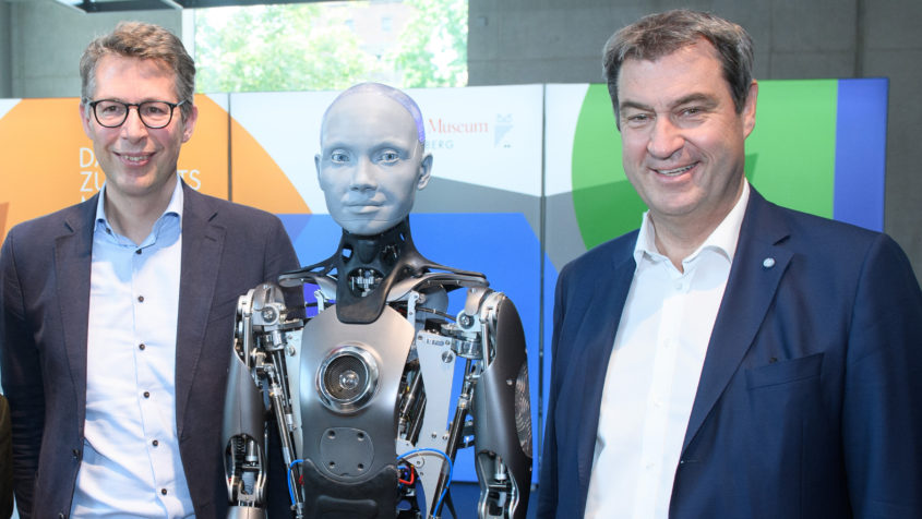 Ministerpräsident Dr. Markus Söder, MdL (rechts), und Wissenschaftsminister Markus Blume, MdL (links), treffen den Humanoide Roboter Ameca (Mitte).