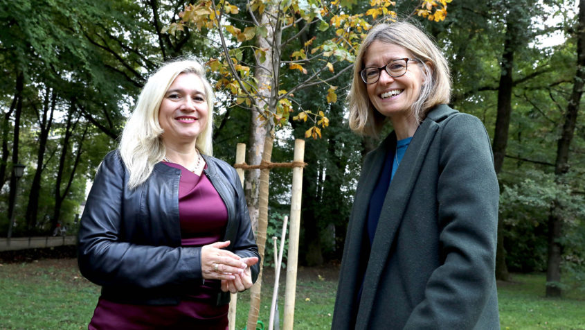 Europaministerin Melanie Huml, MdL (links), und die britische Botschafterin Jill Gallard (rechts), vor der Rosskastanie im Englischen Garten.