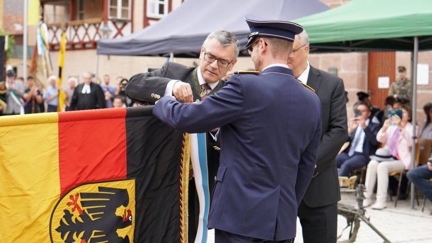 Anlässlich des 60-jährigen Bestehens der Patenschaft zwischen der 7. Kompanie des Luftwaffenausbildungsbataillons und der Stadt Heideck überreicht Staatsminister Dr. Florian Herrmann ein Fahnenband des Bayerischen Ministerpräsidenten.