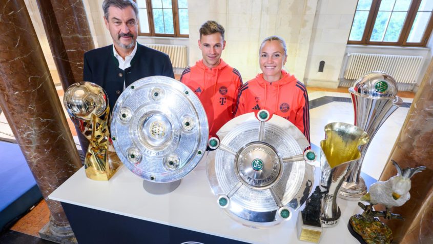 Gruppenbild (v.l.n.r.): Ministerpräsident Dr. Markus Söder, Joshua Kimmich und Glódís Perla Víggósdottir mit den gewonnenen Pokalen der Frauen- und Herrenfußballmannschaft des FC Bayern München.
