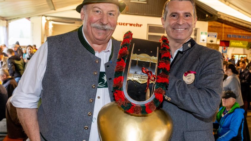 Der Erste Bürgermeister der Gemeinde Balderschwang, Konrad Kienle (links), übergibt Europaminister Eric Beißwenger (rechts) als Gastgeschenk eine Schelle.