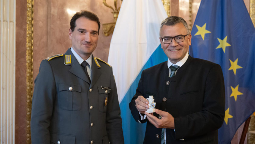 Der Landesvorsitzende des Verbands der Reservisten der Deutschen Bundeswehr e.V. in Bayern, Major d.R. Fabian Forster (links), überreicht Staatsminister Dr. Florian Herrmann (rechts) den Bayerischen Porzellanlöwen im Prinz-Carl-Palais.