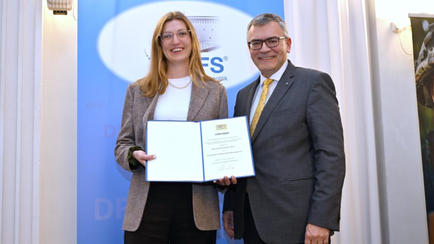 Verleihung des wissenschaftlichen Nachwuchspreises „Aquila ascendens“ des Dialogforums Sicherheitspolitik: Staatsminister Dr. Florian Herrmann (rechts) überreicht den Sonderpreis des Bayerischen Ministerpräsidenten an Jennifer Fetscher (links) für ihre Masterarbeit 'Warfare in the Digital Age – Analyzing the Impact of DDoS Attacks on Battlefield Events in the Ukraine War'.