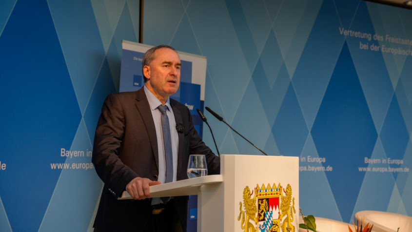 Minister Aiwanger hält seine Begrüßung am Stehpult, auf dem das Staatswappen zu sehen ist. Im Hintergrund sieht man die Rautenwand der Vertretung.