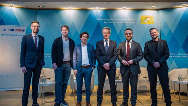 Die sechs Herren stehen auf der B&uuml;hne zum Gruppenfoto. Im Hintergrund sind blaue Rauten sowie das Staatswappen und wei&szlig;e Sessel zu sehen.