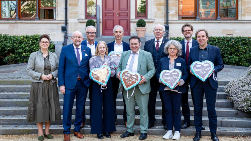 Zehn Personen stehen vor der Bayerischen Vertretung in Brüssel und halten weiß-blaue Lebkuchenherzen in der Hand.