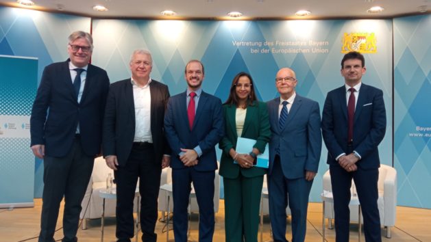 F&uuml;nf Personen stehen auf einem Podium vor blau-wei&szlig;en Rauten. Im Hintergrund ist das Staatswappen zu erkennen.